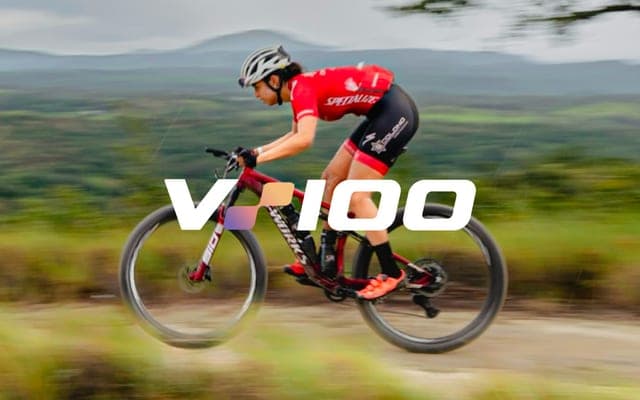 A mountain biker in a red Specialized kit, motion-blurred at speed, with the V100 logo across the frame